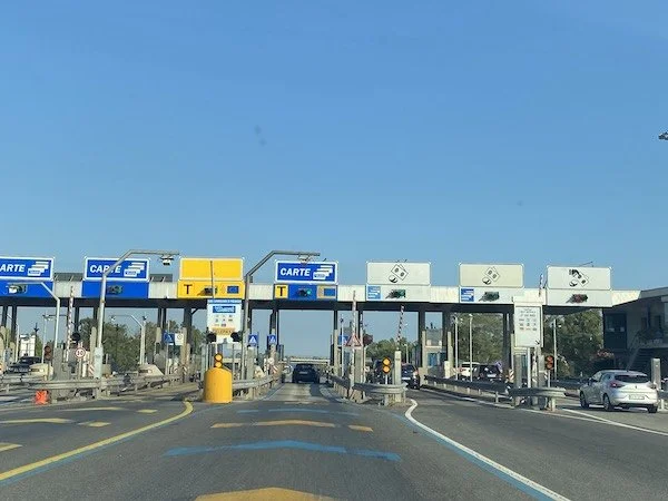 Toll booth with multiple lanes and signs, cars passing through on a sunny day.