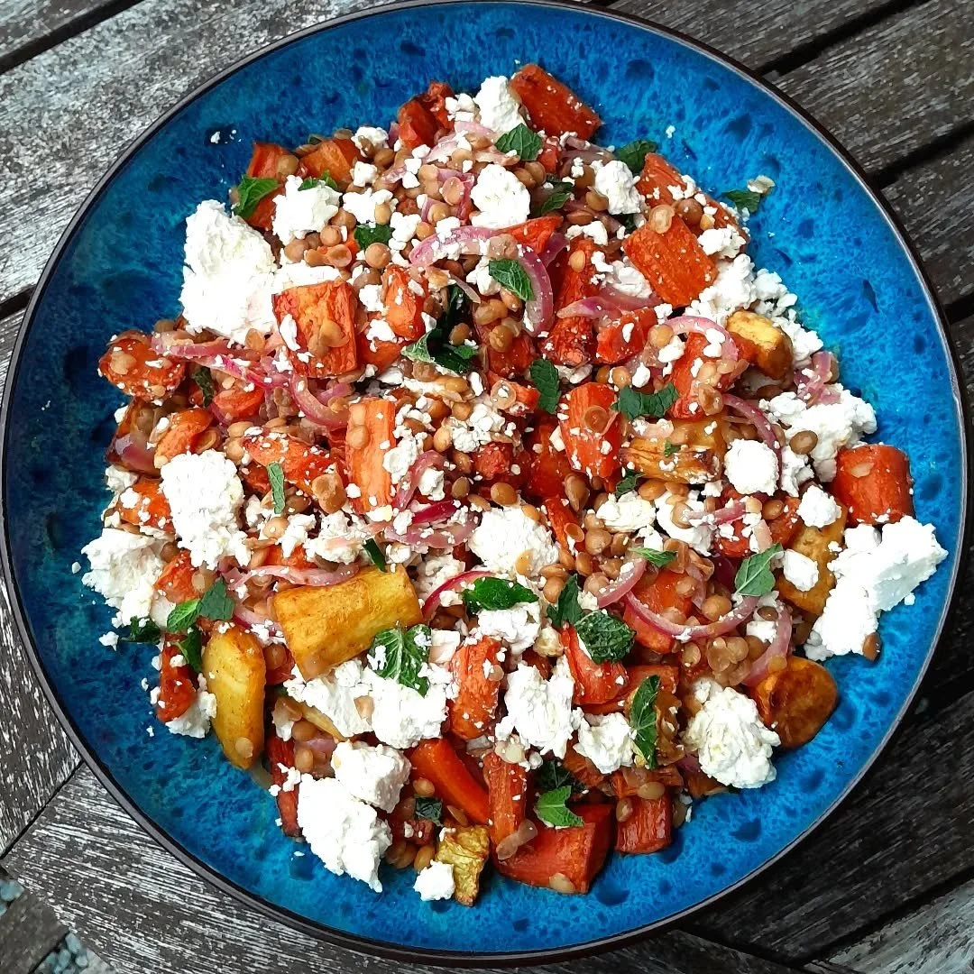 A vibrant salad with roasted vegetables, lentils, crumbled feta cheese, and fresh herbs on a blue plate.