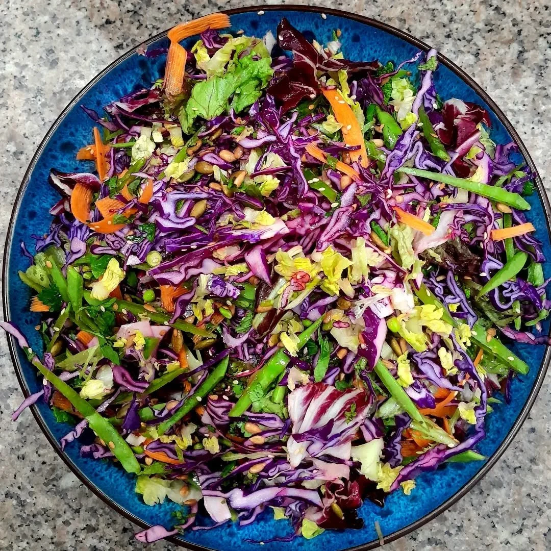 A colorful bowl of shredded cabbage salad with carrots, greens, sunflower seeds, and sesame seeds on top.