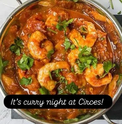 A pot of shrimp cooked in a spicy tomato-based curry with fresh cilantro, featuring visible shrimp and chunks of vegetables.