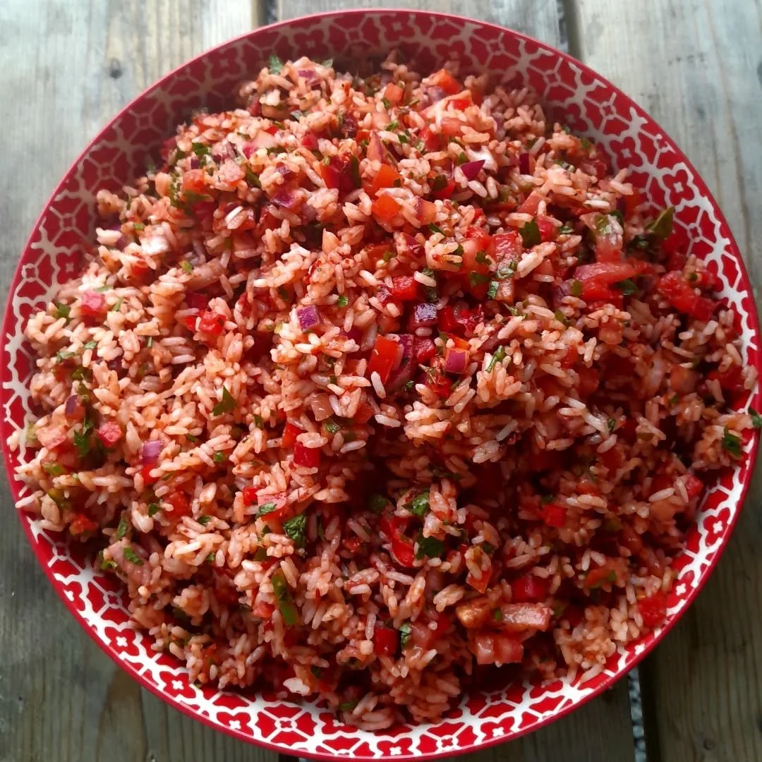 A bowl of fried rice mixed with chopped vegetables like red peppers, green onions, and onions on a wooden surface.