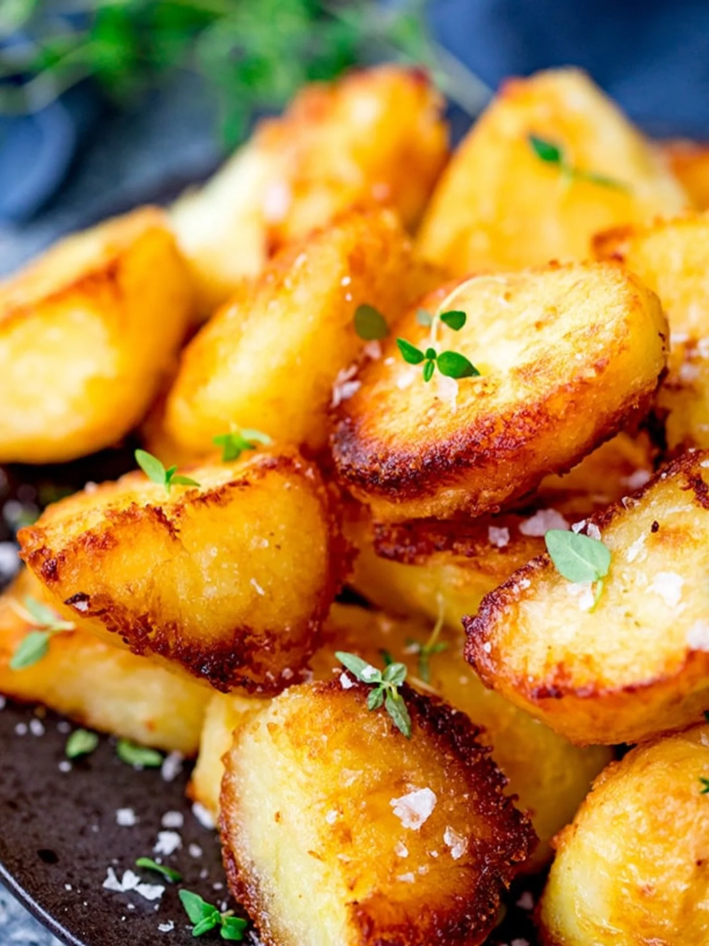 Golden roasted potato pieces garnished with green herbs and salt on a black surface.