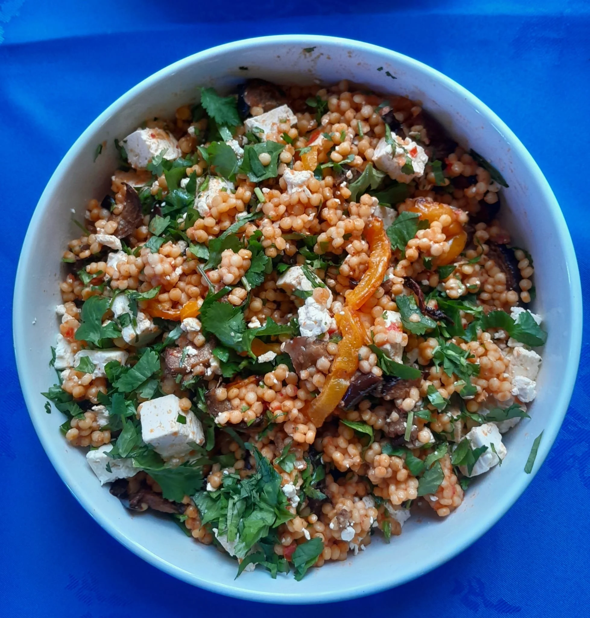 A bowl of couscous salad with vegetables, feta cheese, and chopped herbs.