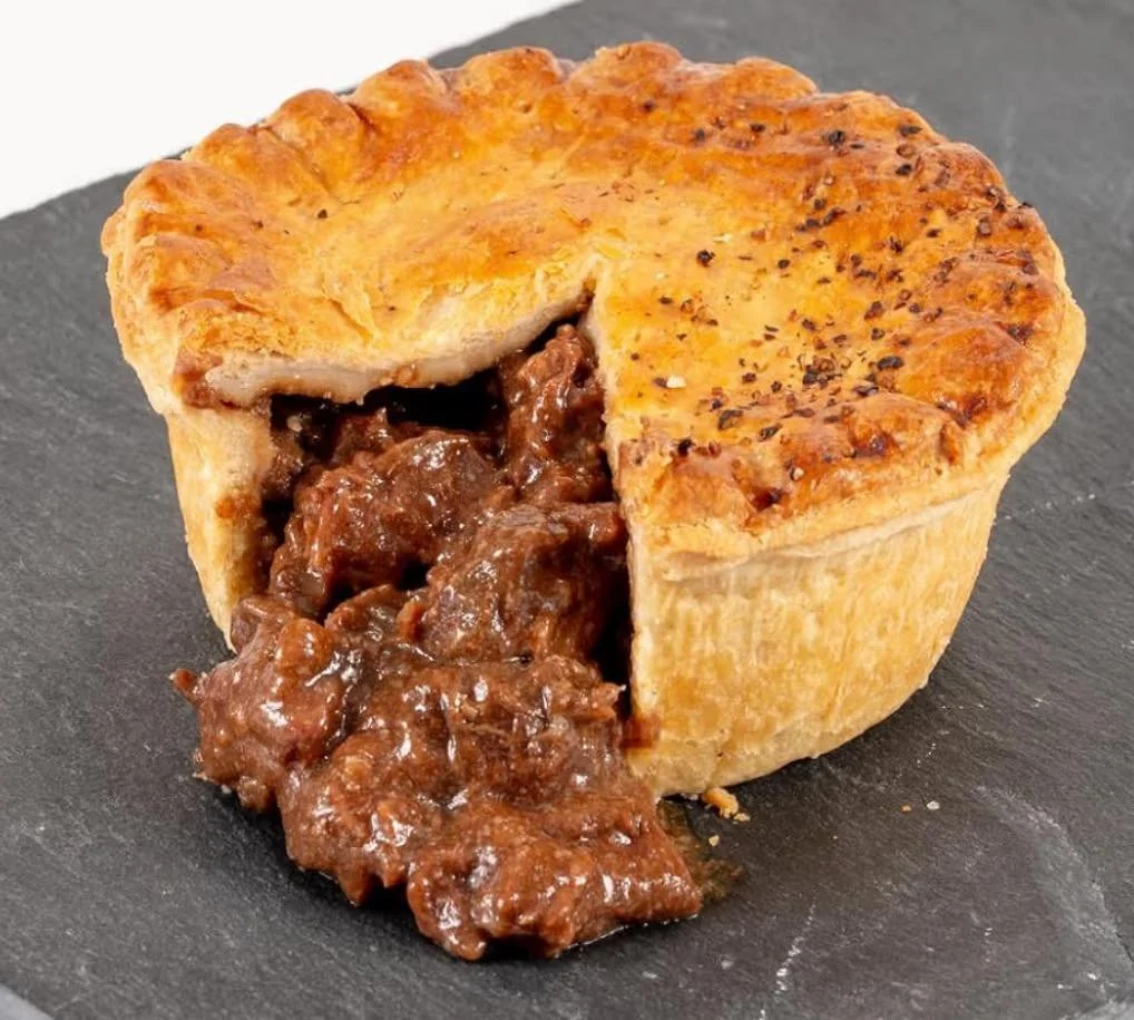 A savory meat pie with a flaky golden crust, partially cut open to reveal rich, beef stew filling inside, placed on a black slate serving board.