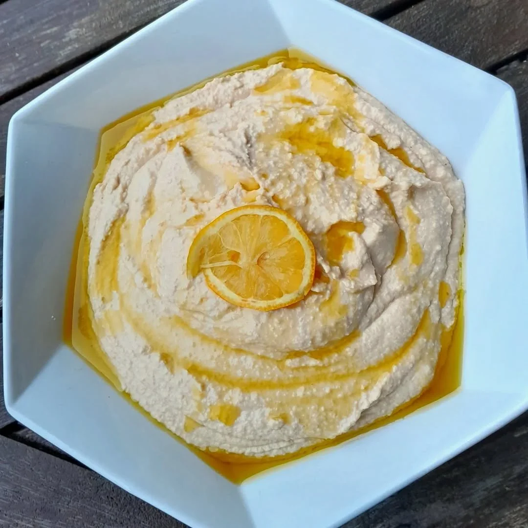 Lemon hummus garnished with lemon slices and drizzled with olive oil in a white bowl on a wooden surface.