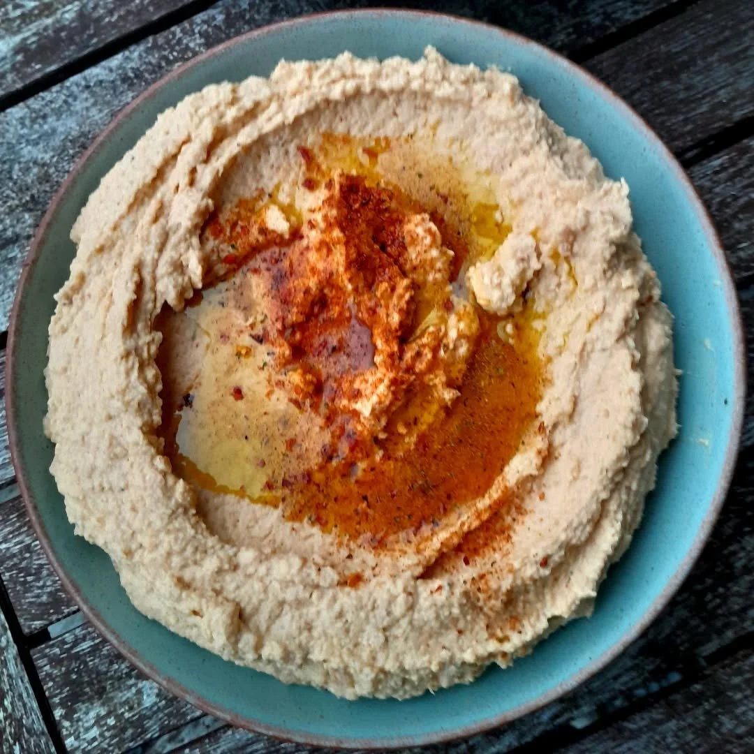 A bowl of hummus topped with olive oil, paprika, and spices on a wooden surface.