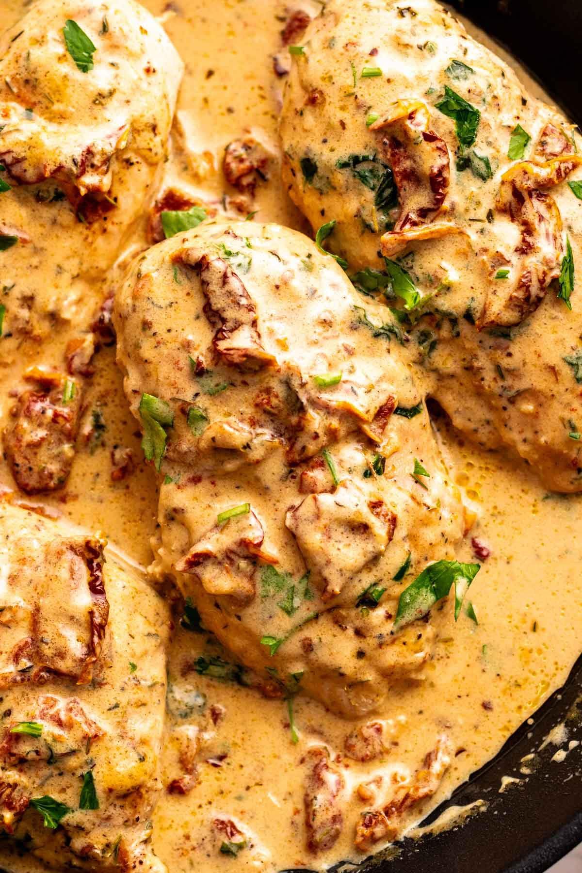 Close-up of cooked chicken breasts in creamy sauce with herbs and chopped bacon.