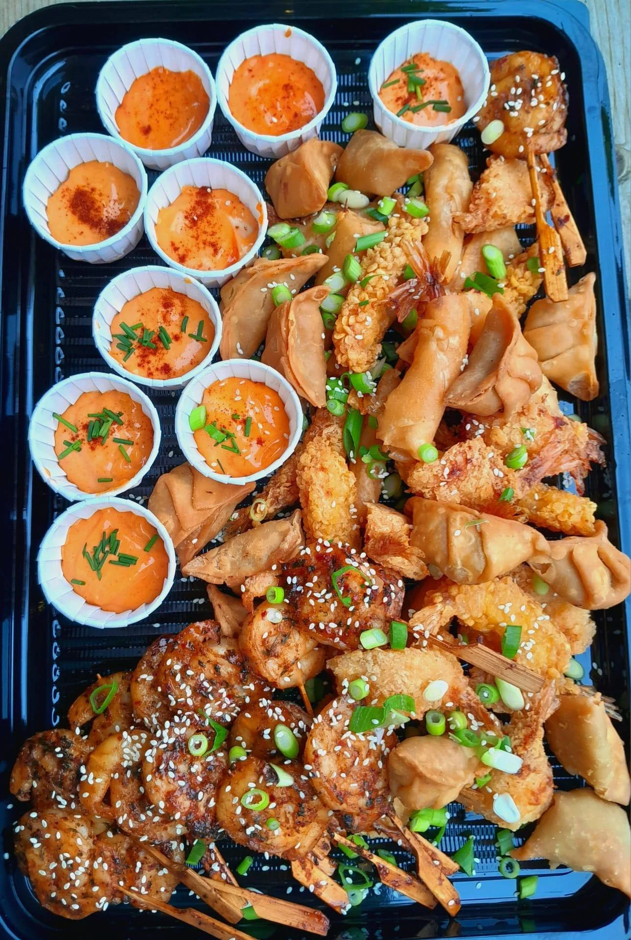 Assorted Asian appetizers including mini egg custards, spring rolls, chicken wings, fried shrimp, and skewered shrimp garnished with green onions and sesame seeds.