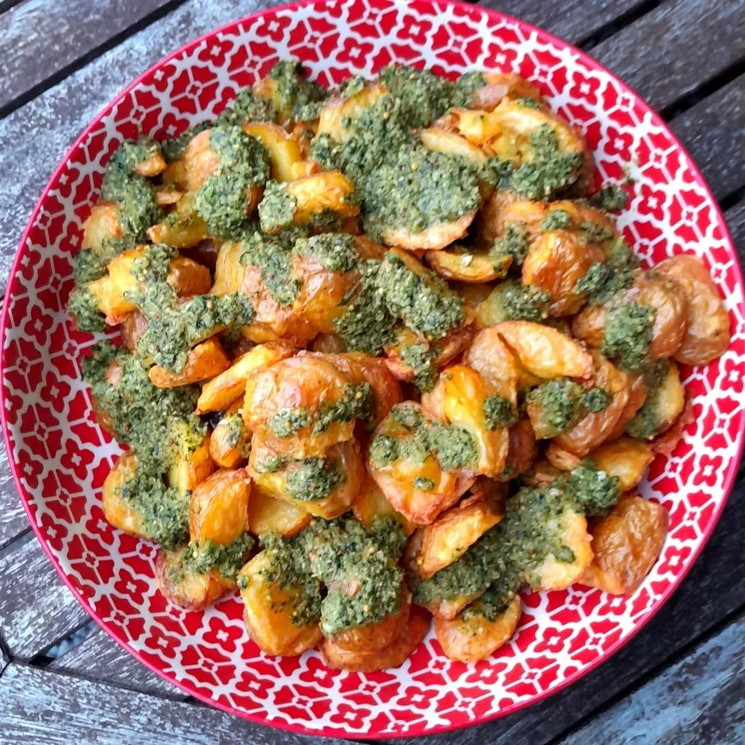 Plate of cooked chicken with green pesto sauce on top, placed on a wooden surface.