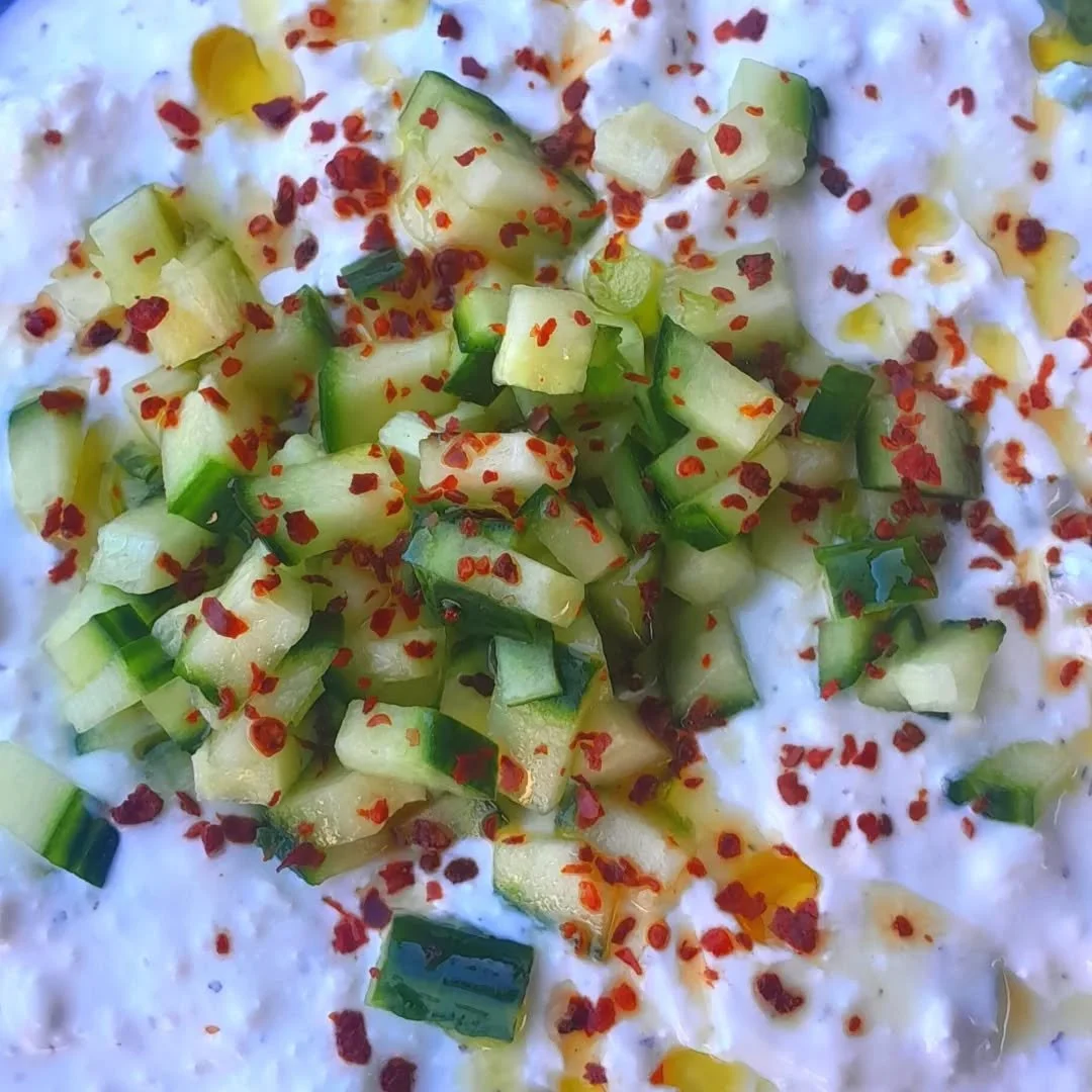 Chopped cucumbers sprinkled with red pepper flakes on a creamy white base, possibly yogurt or sour cream, with a drizzle of olive oil.