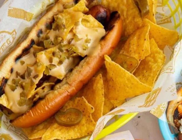 Hot dog with mustard and relish, served with nacho chips in a basket.