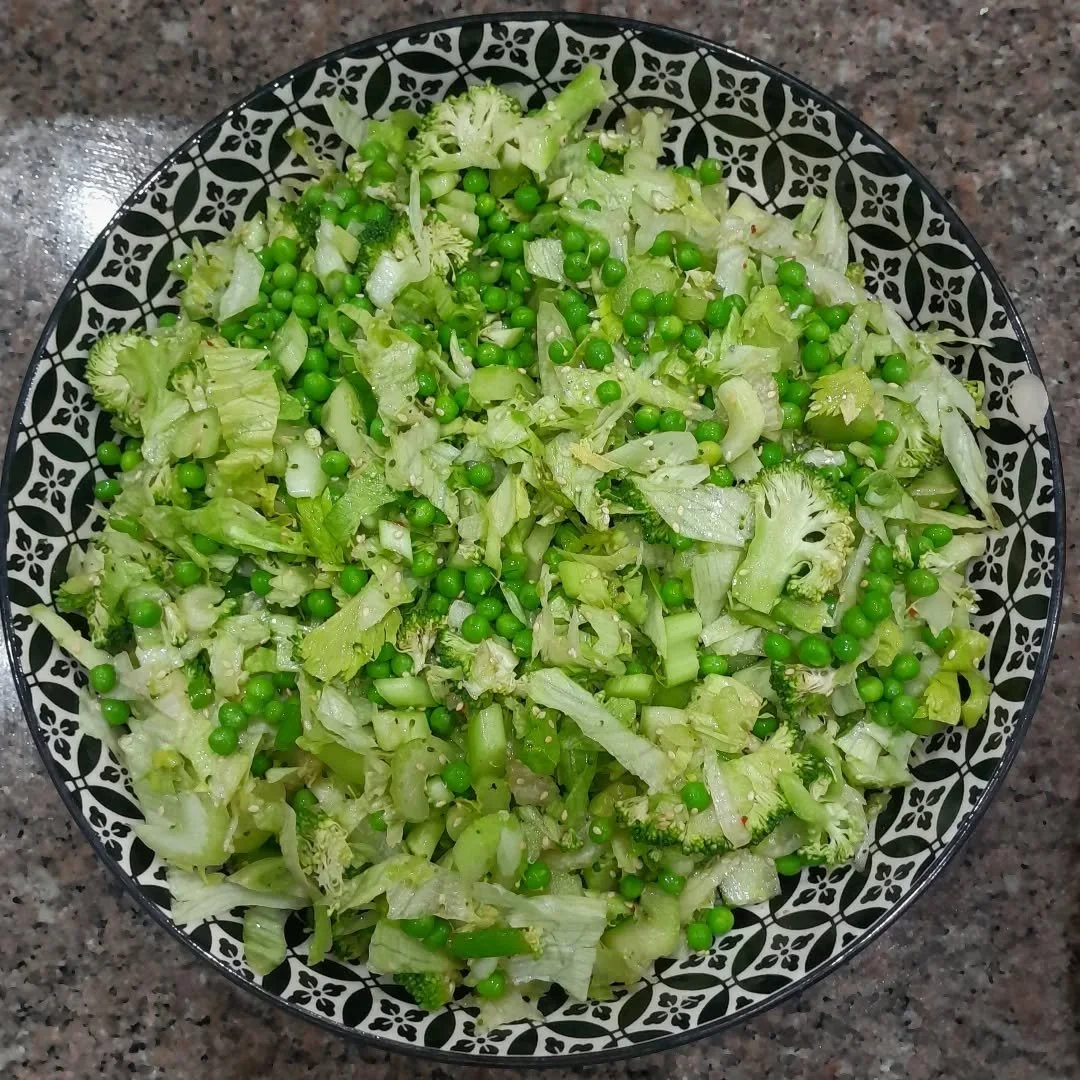 A bowl of chopped lettuce and green peas on a granite countertop.