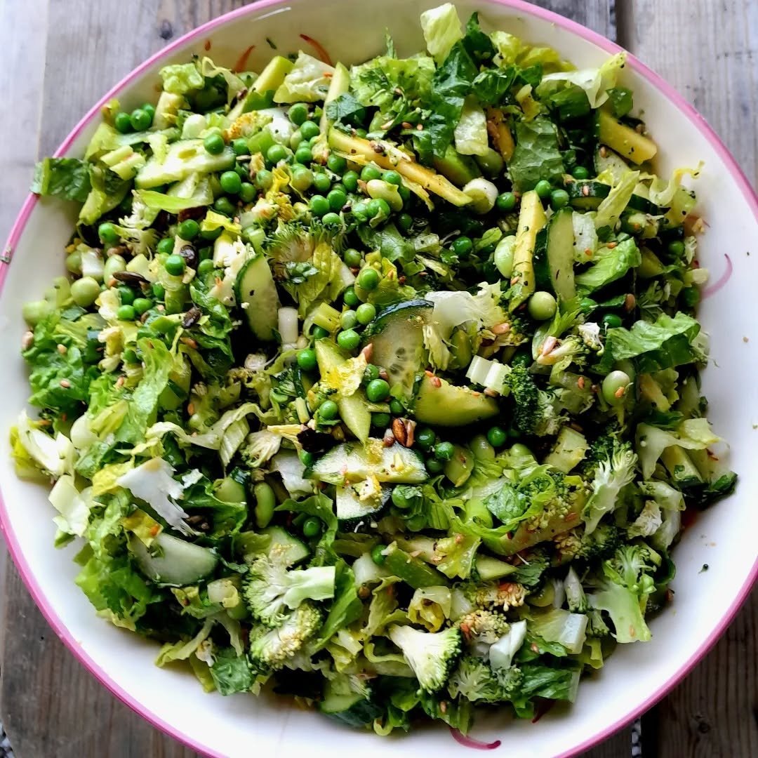 Mixed chopped green vegetables with peas in a white bowl with a pink rim, on a wooden surface.