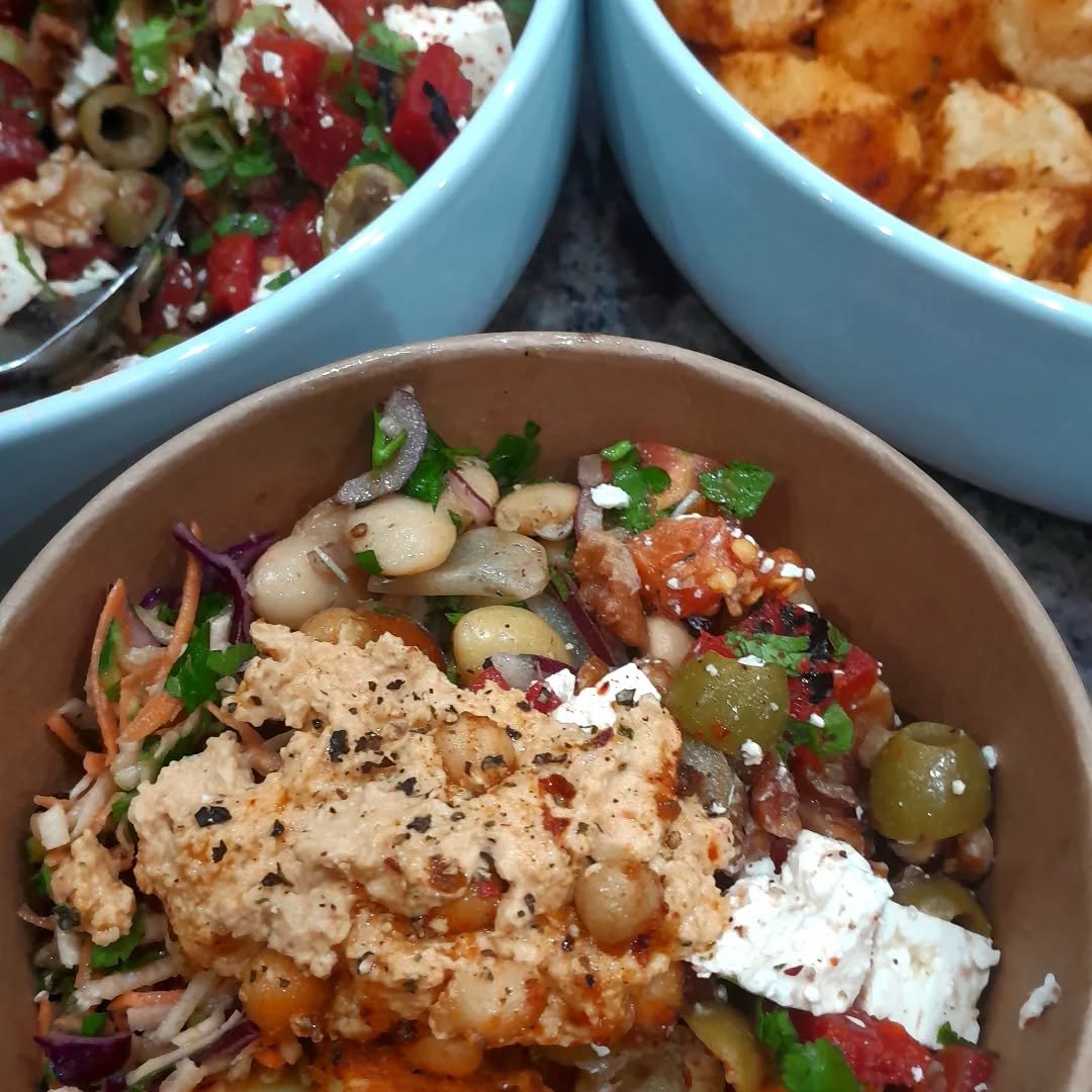 Close-up of a bowl of chickpea salad with vegetables, topped with crumbled cheese and black pepper, with two other bowls of food in the background.