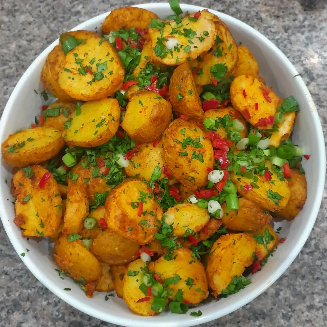 Bowl of spicy roasted potatoes garnished with chopped green onions and red chili flakes.