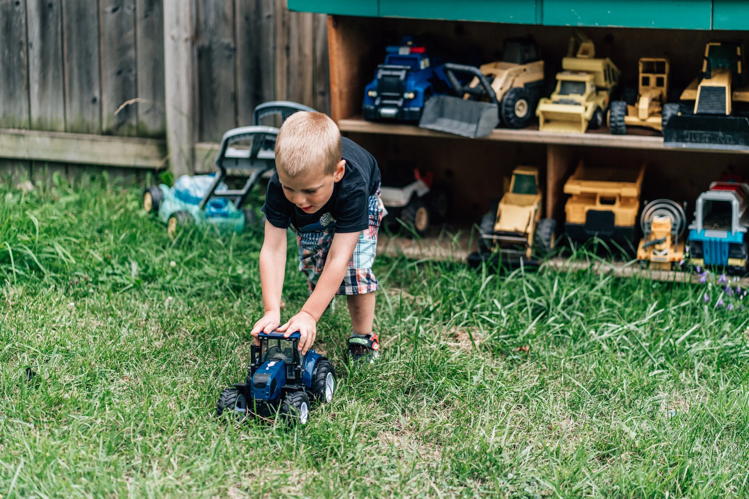 Boy pushing a toy tractor through the grass at the Belleville Outdoor Preschool