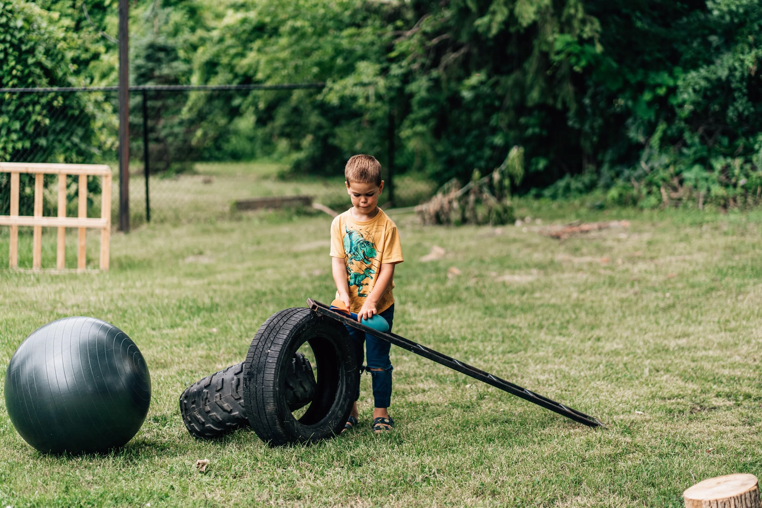 Boy in yellow shirt playing with tires and a metal ladder at the Belleville Outdoor Preschool