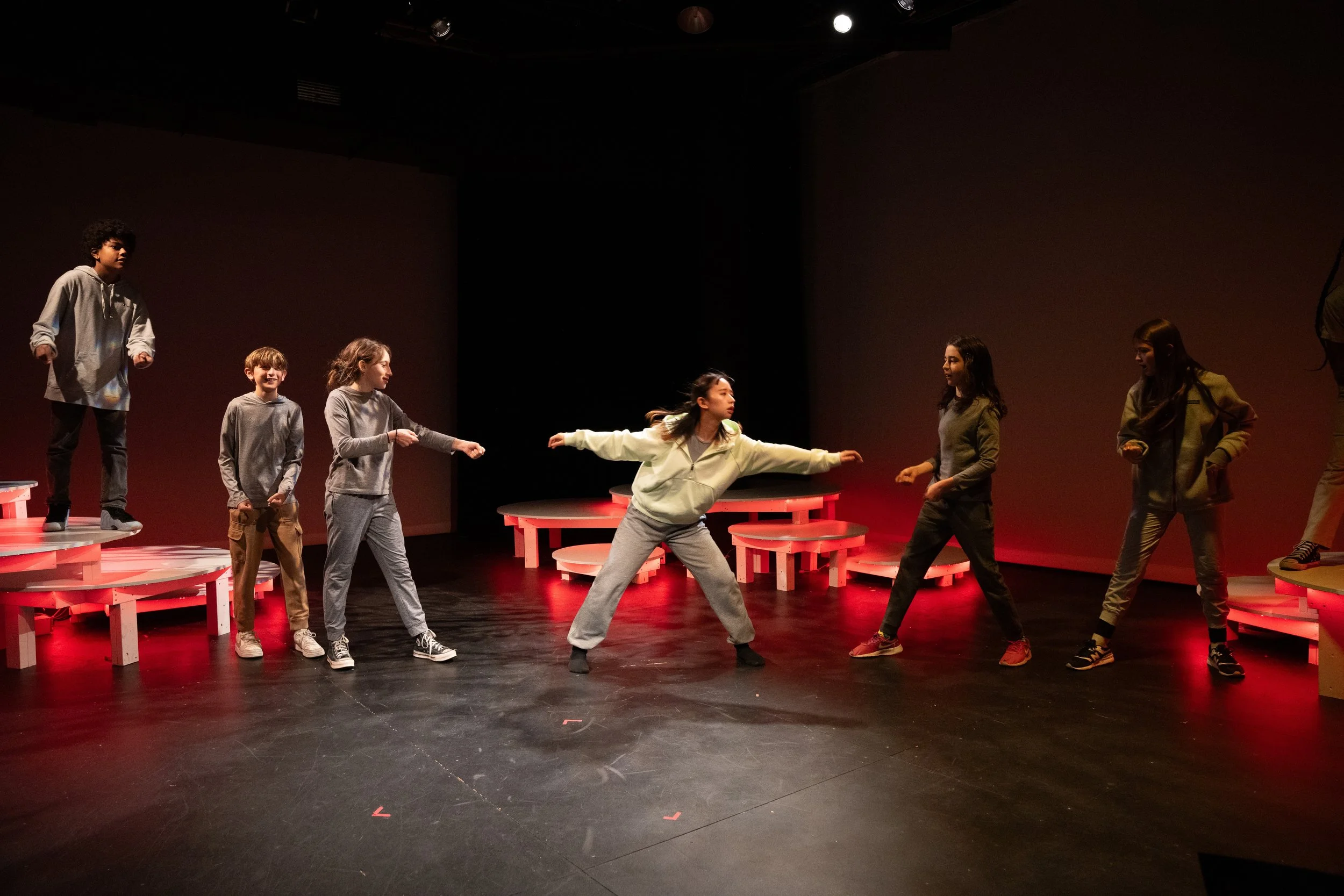 Children performing on a stage with red circular platforms and a dark background.