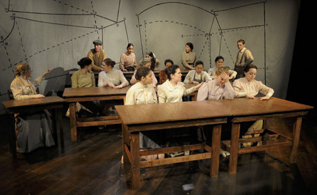 A scene from the musical "The Sound of Music" with actors portraying the von Trapp family, seated at wooden tables on a stage with a backdrop featuring musical note and star outlines.