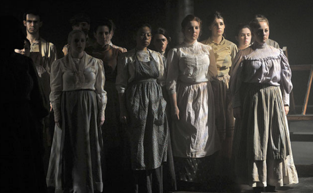 A group of women in historical clothing standing in a dimly lit room.