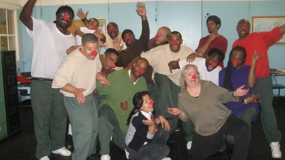 Group of people with red clown noses posing together in a room, some standing, some kneeling, making playful gestures.