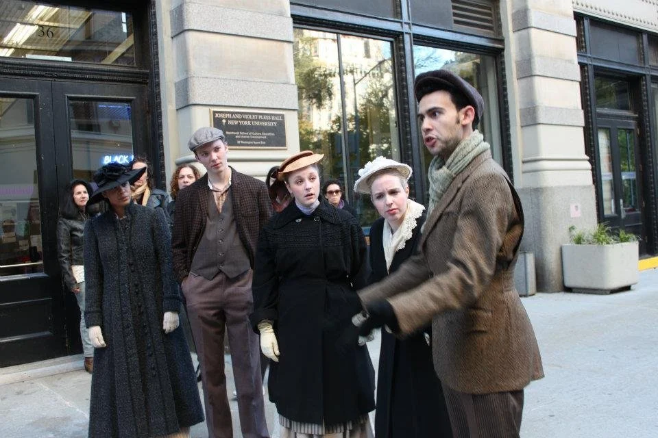 Group of people dressed in vintage clothing standing outside a building with a sign that reads 'Joseph and Violet Pleas Hall, New York University'.