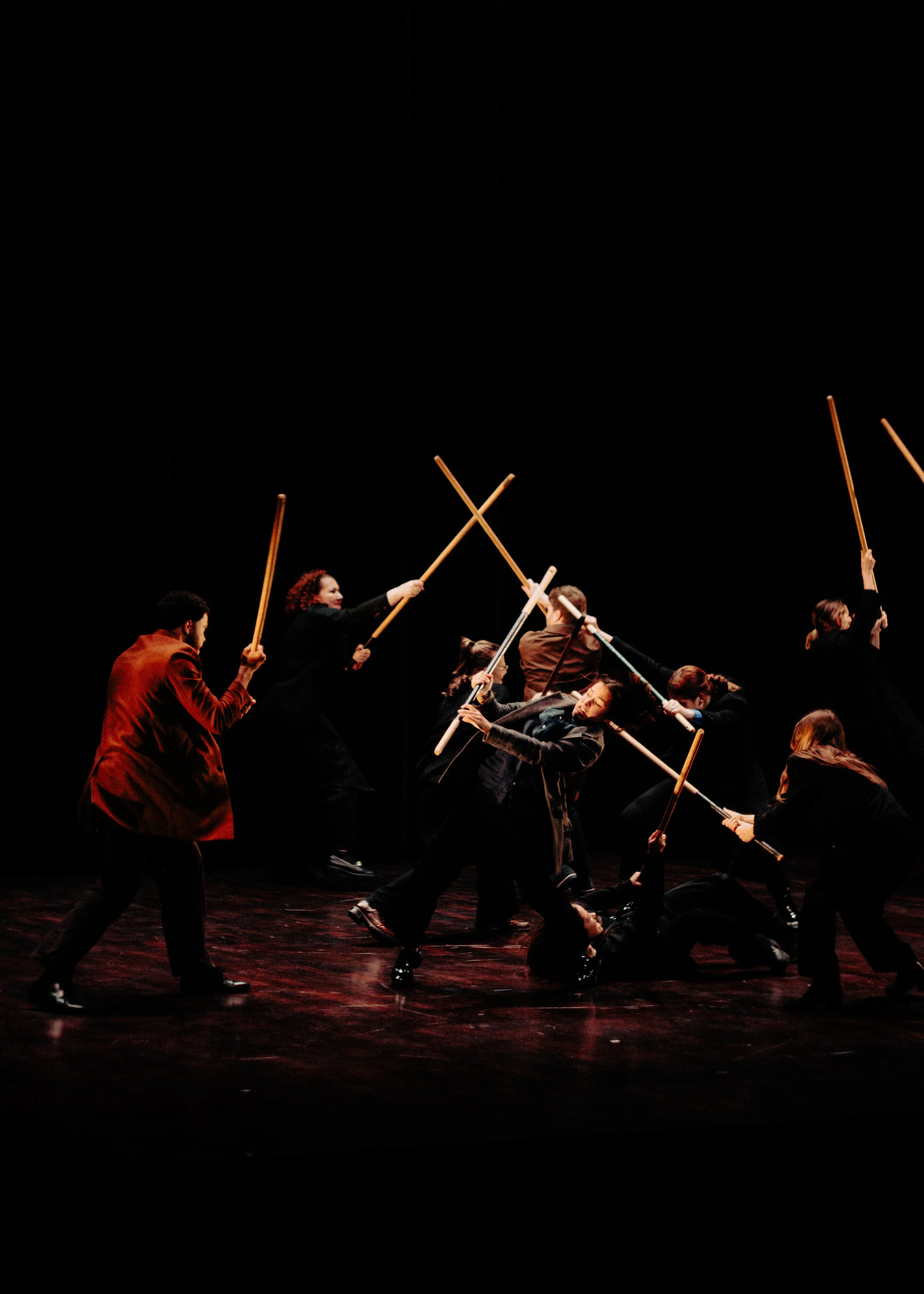 Une scène de danse ou de théâtre avec plusieurs personnes tenant des bâtons, dans un espace sombre.