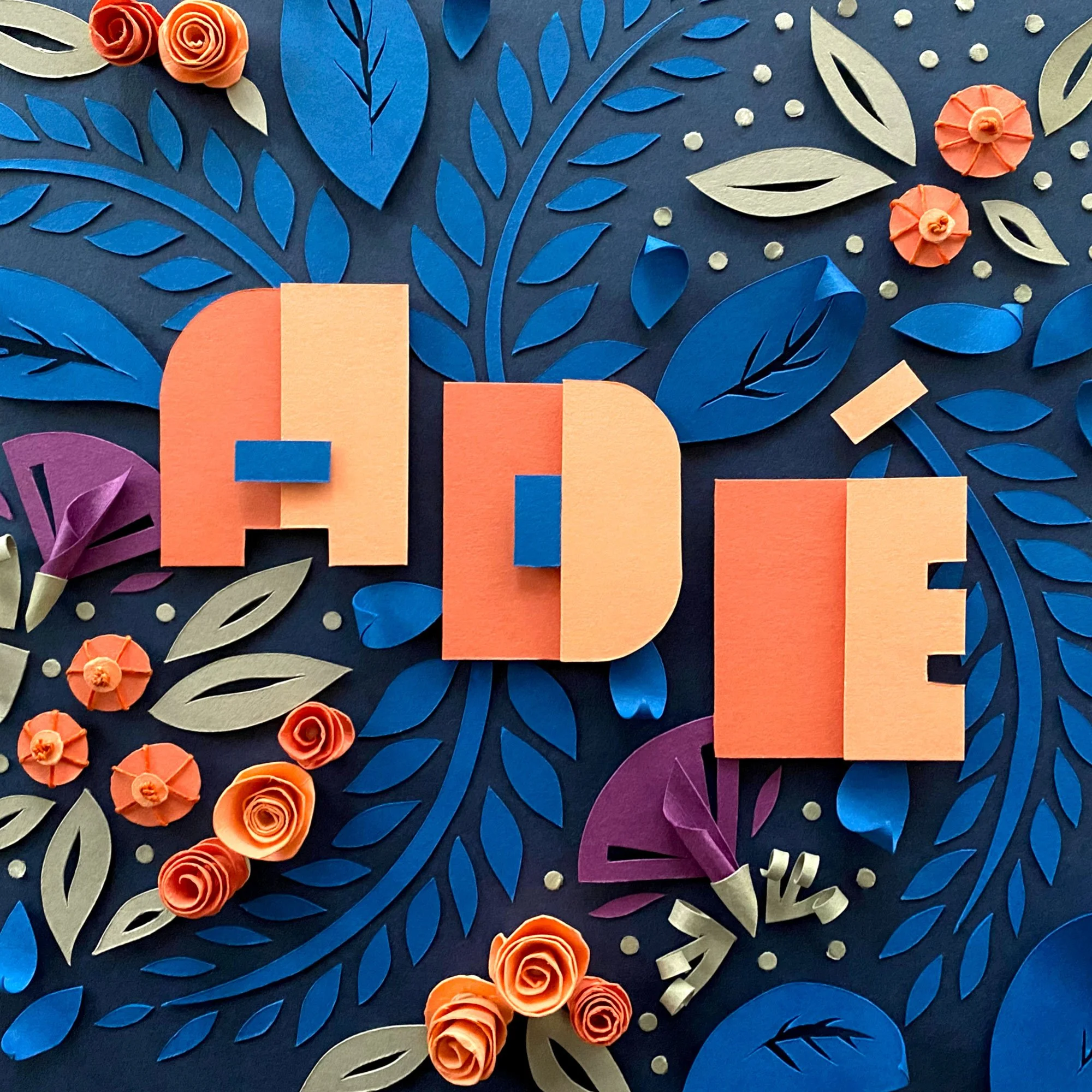 Colorful paper craft spelling the word 'ADD' with decorative paper flowers and leaves on a dark background.