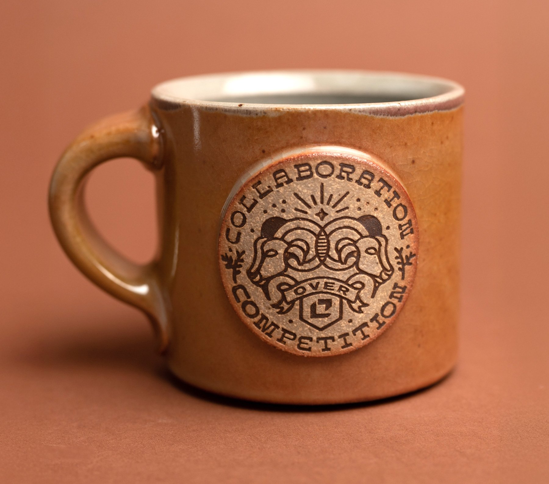 A ceramic coffee mug with a logo reading 'Cellaration Coffee' and featuring a design of two ram's heads facing each other with a banner that says 'Cover 2' amidst a circular emblem.
