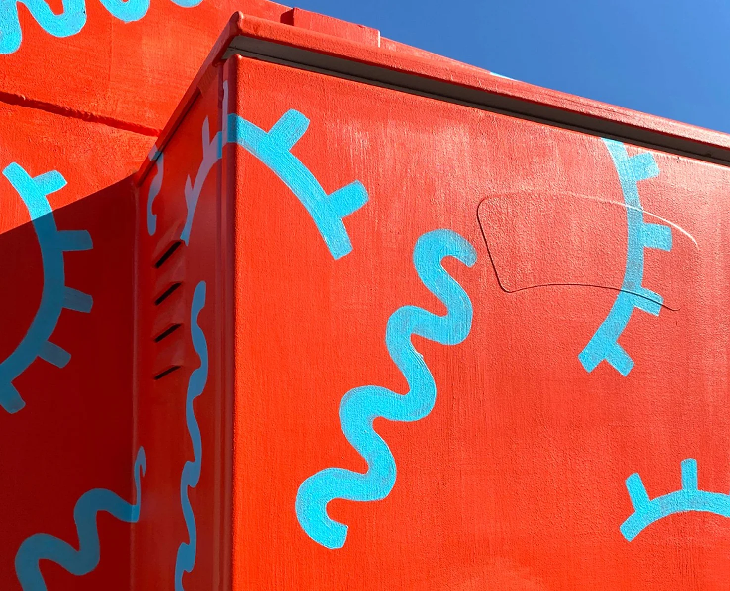 Close-up of a red building with painted blue and light blue abstract clock and wave-like designs.