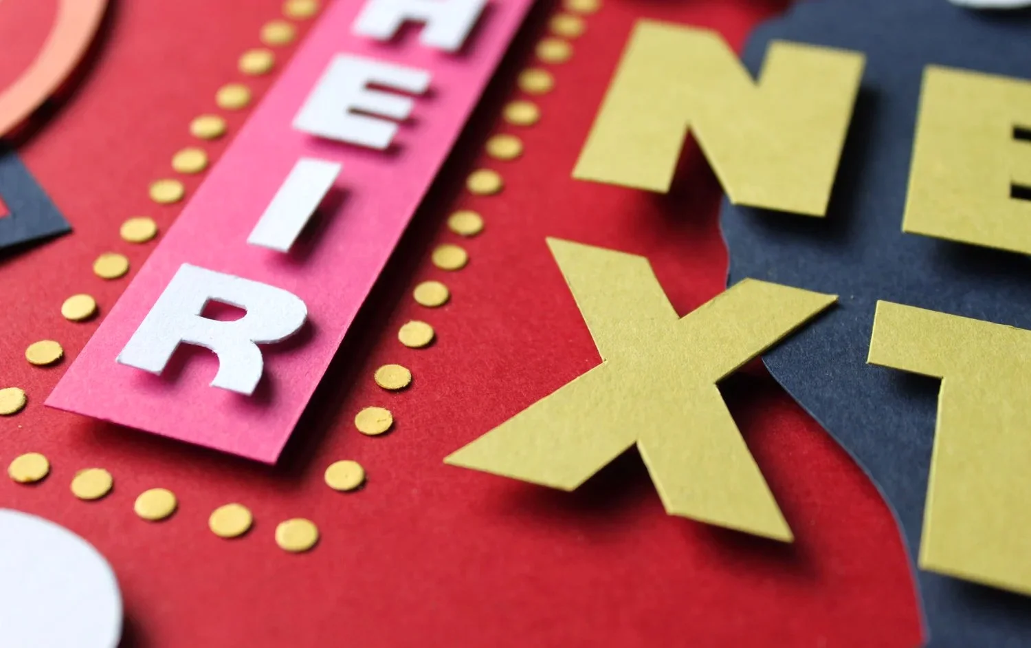 Close-up of a colorful, layered paper craft featuring letters and designs, with the words 'HAPPY' and 'X' visible.