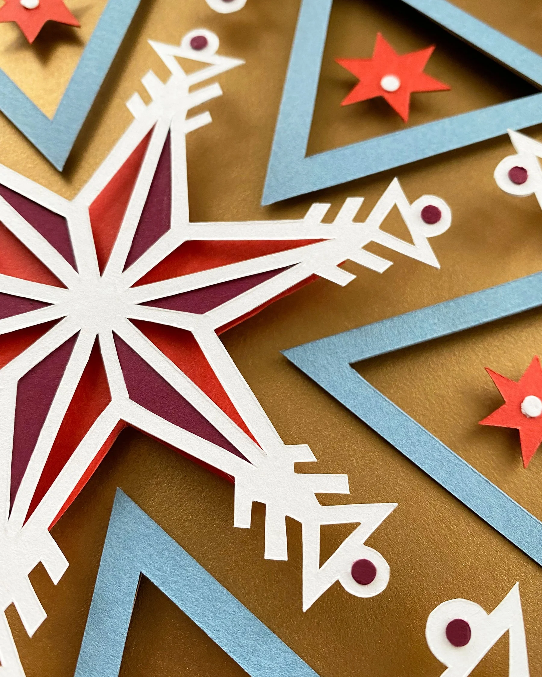 Close-up of colorful paper cutouts of various shapes including stars and snowflakes on a golden background, possibly holiday decorations.