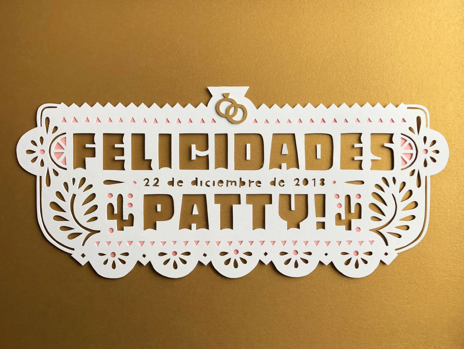 Decorative paper cutout celebrating a wedding, with the names Fidelidad and Patty, date December 22, 2018, on a gold background.