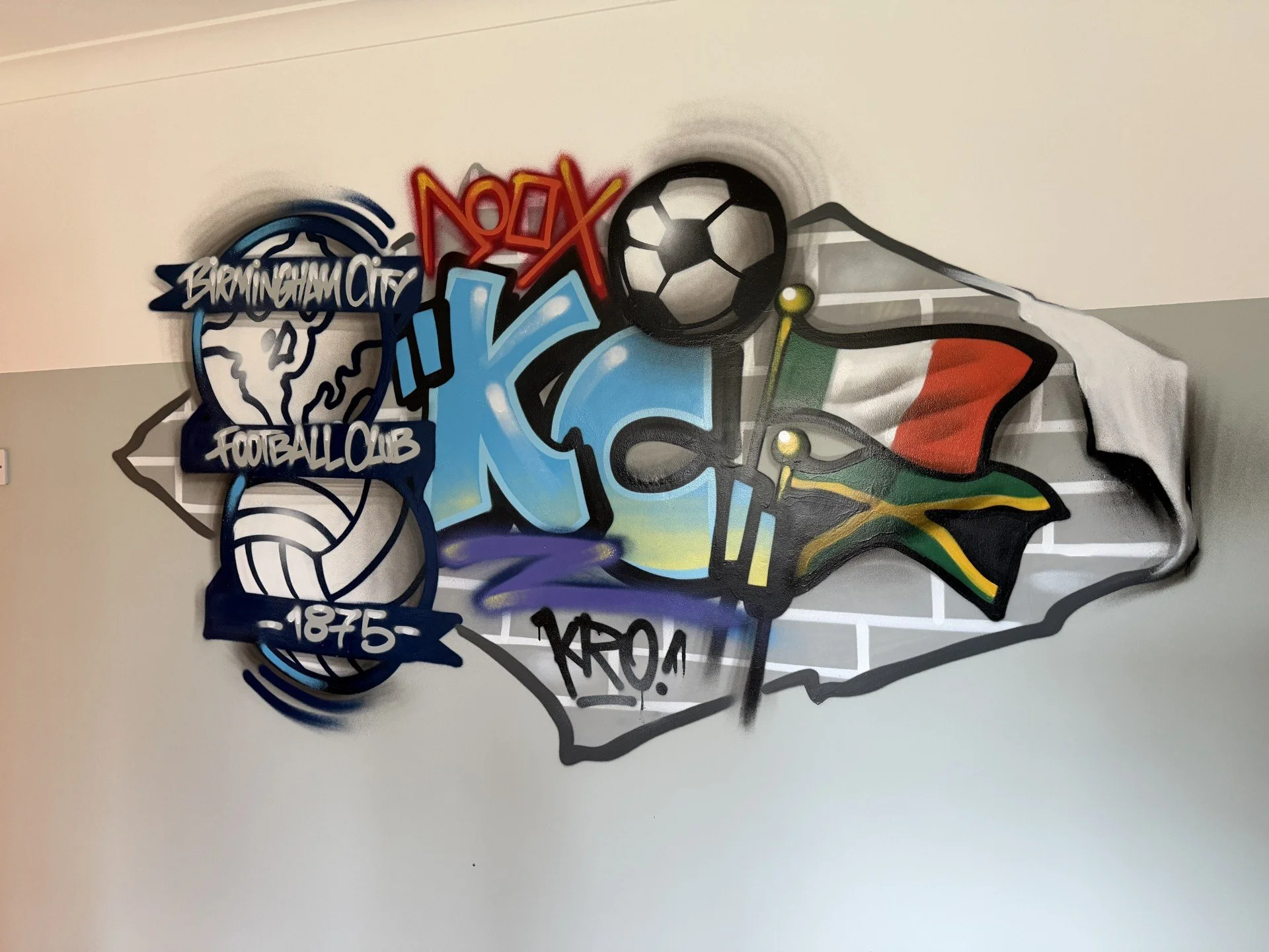 Graffiti mural of Birmingham City Football Club emblem with a soccer ball, the Jamaican flag, and the Italian flag, on a brick wall.