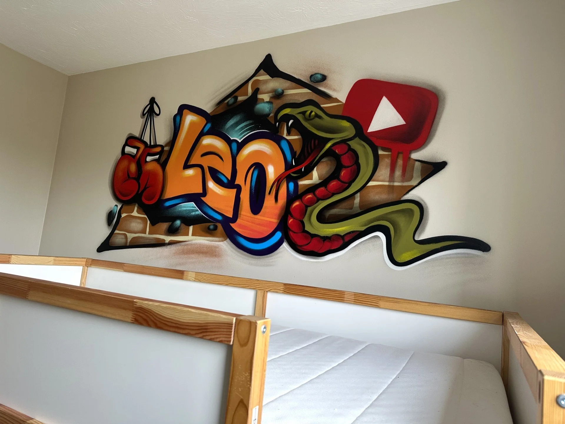 Graffiti art on a wall with a boxing glove hanging from the letter L, a snake with open mouth, and a YouTube play button symbol.