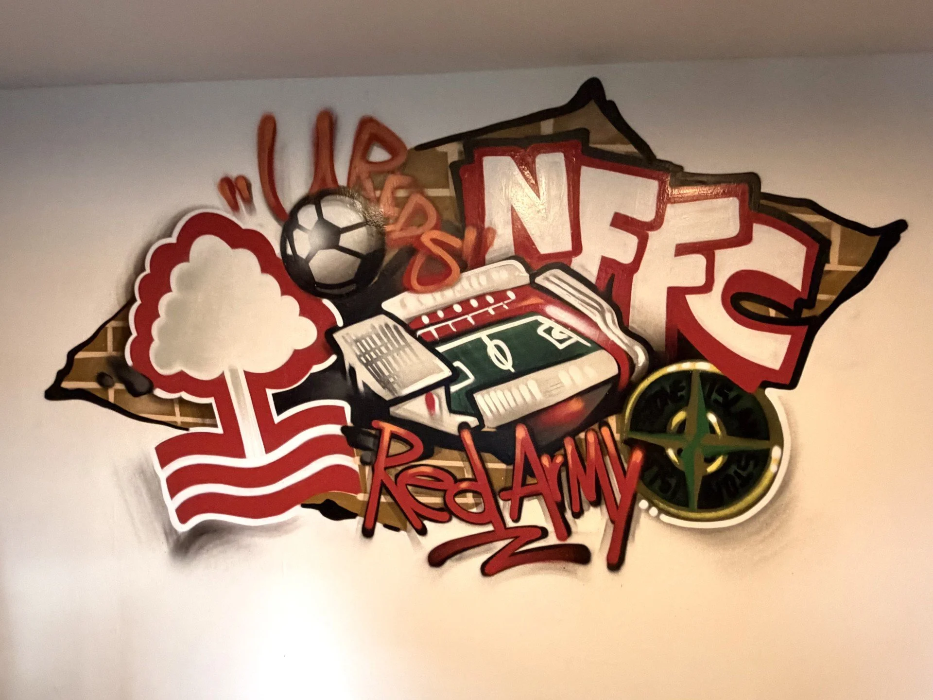Decorative wall art celebrating Nebraska. Features a football field, a soccer ball, a tree, a compass, and words like 'Nebraska,' 'Red Army,' and 'U.S.' with a brick background outline.