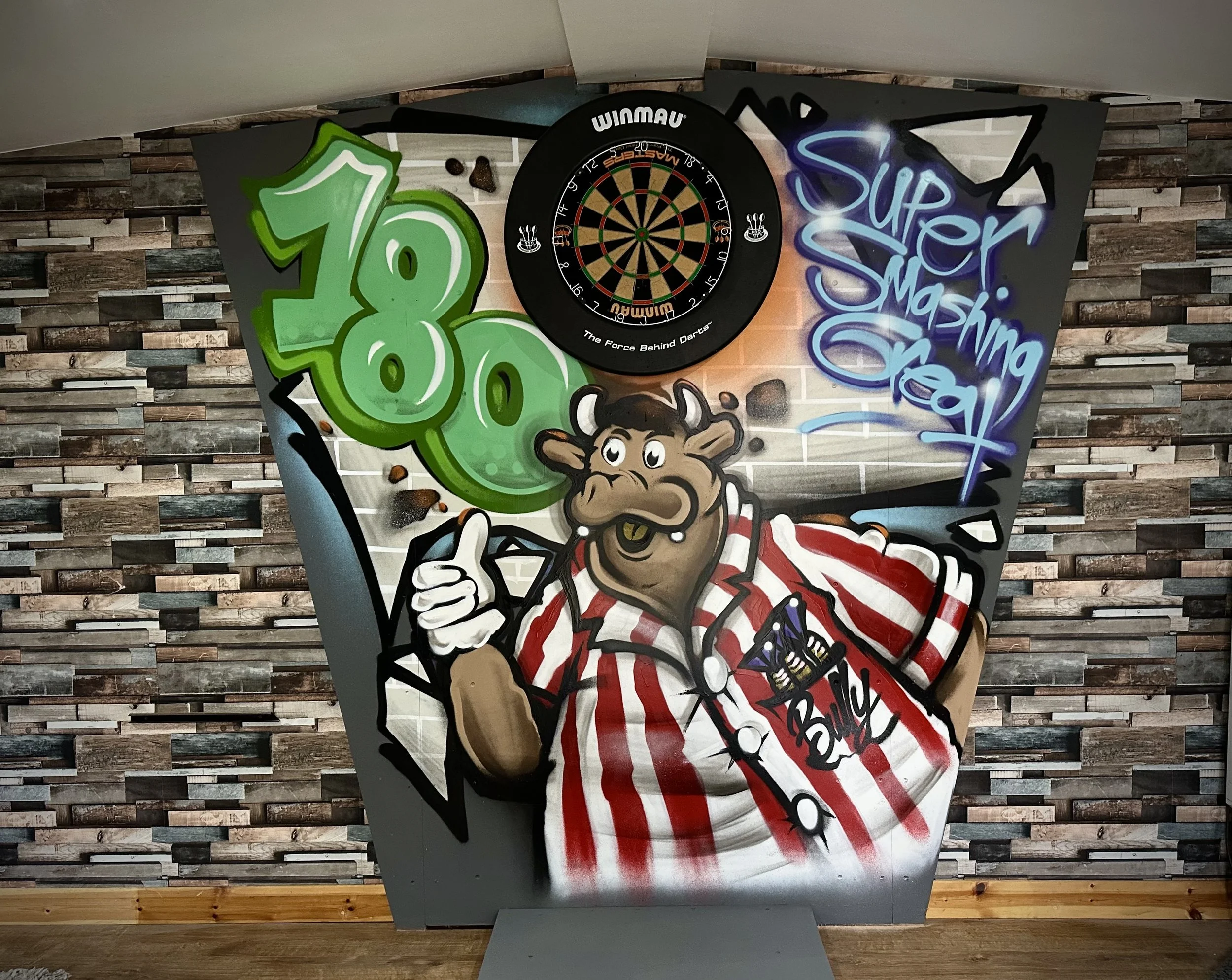 Graffiti mural featuring a cartoon bull wearing a red and white striped shirt, giving a thumbs up, with green '18' graffiti and a dartboard above it. The mural includes a blue graffiti tag that says 'Super Masking Head'. The background has a brick wall pattern.