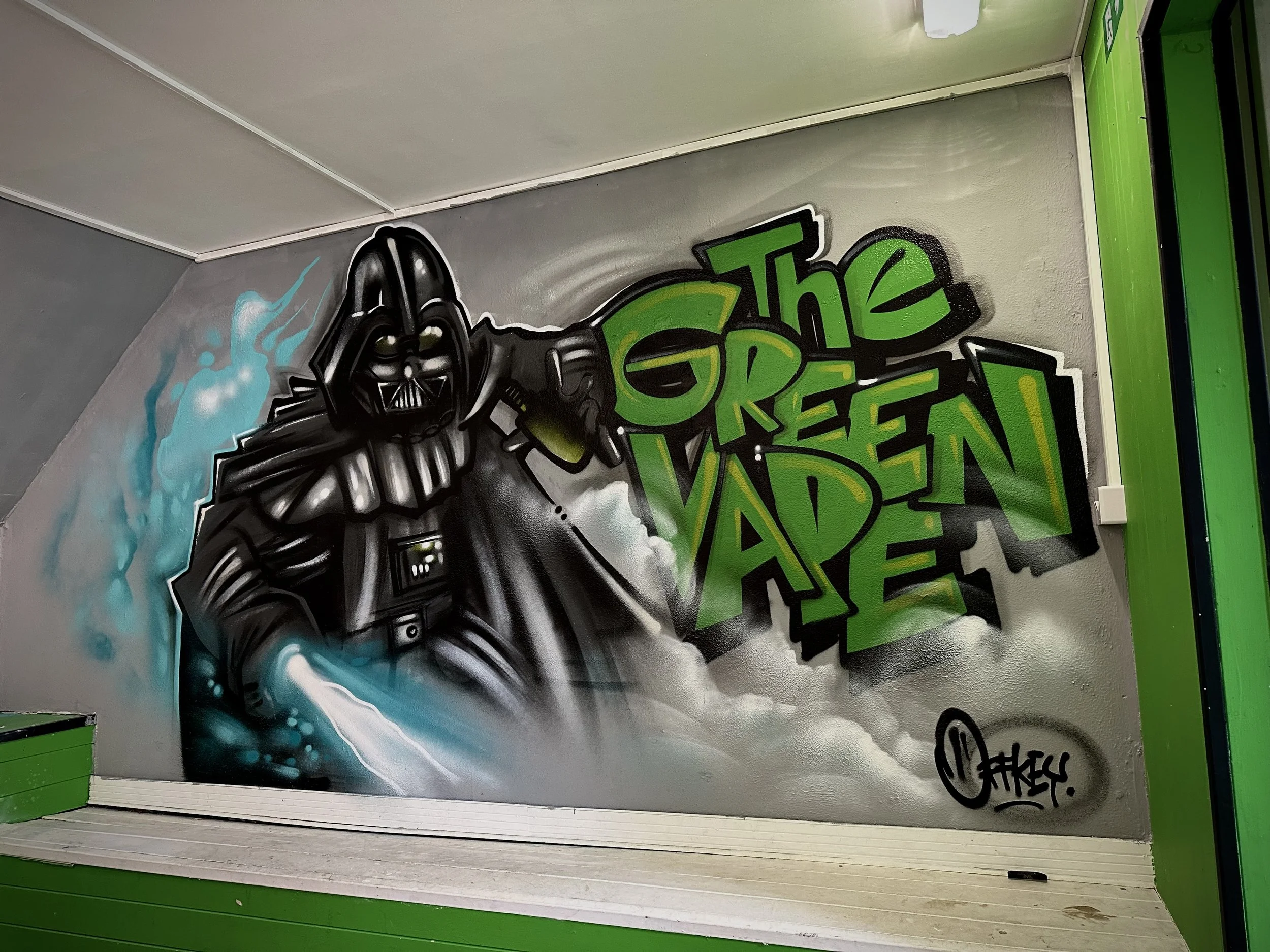 Graffiti artwork of Darth Vader from Star Wars holding a glowing lightsaber, with the words 'The Green Vader' in bold green letters beside him.