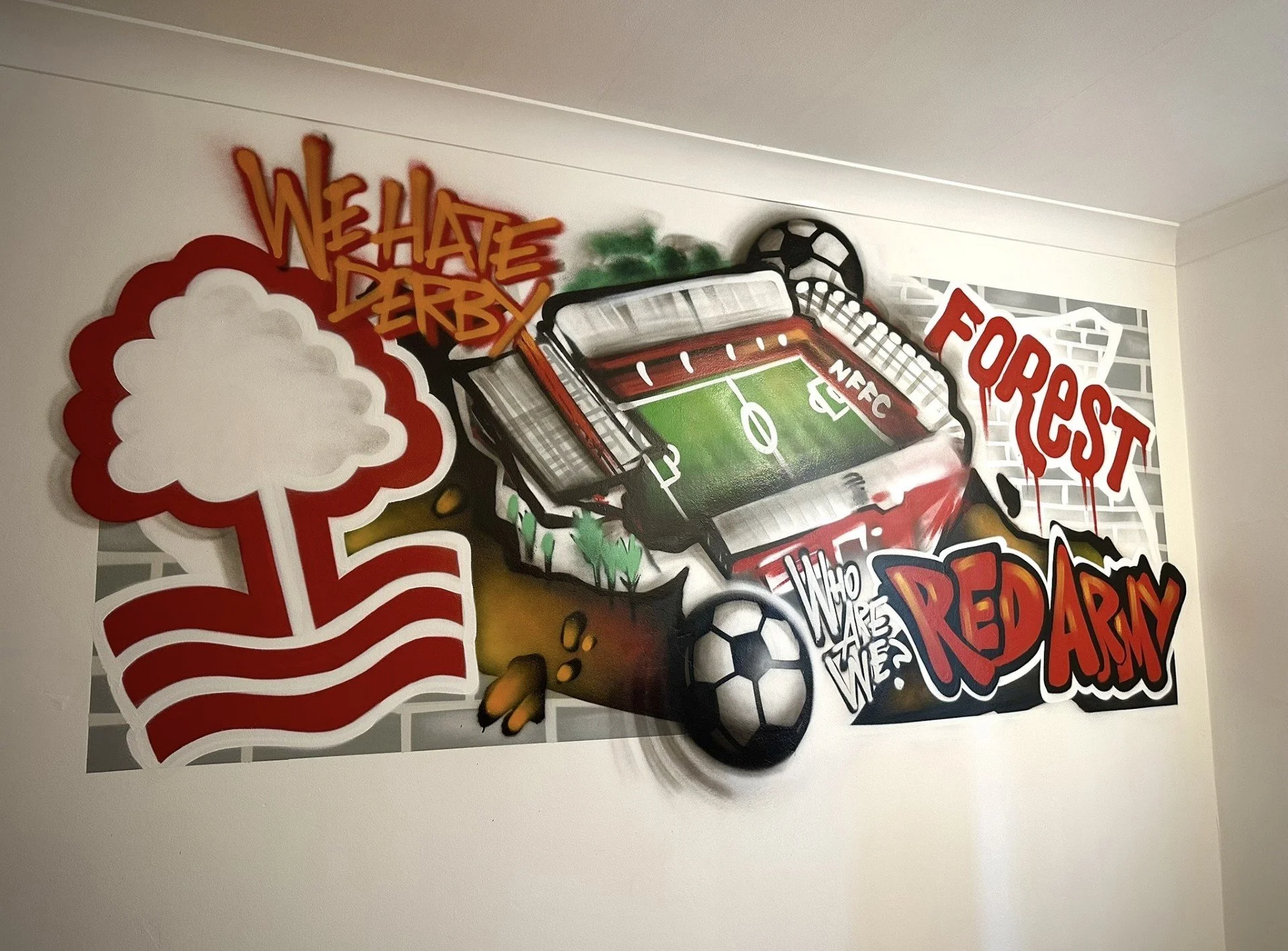 Graffiti art of a football stadium with soccer balls, spray paint, and words like 'WE HAVE DERBY,' 'FORREST,' 'WHO ARE WE,' and 'RED ARM' on a wall.