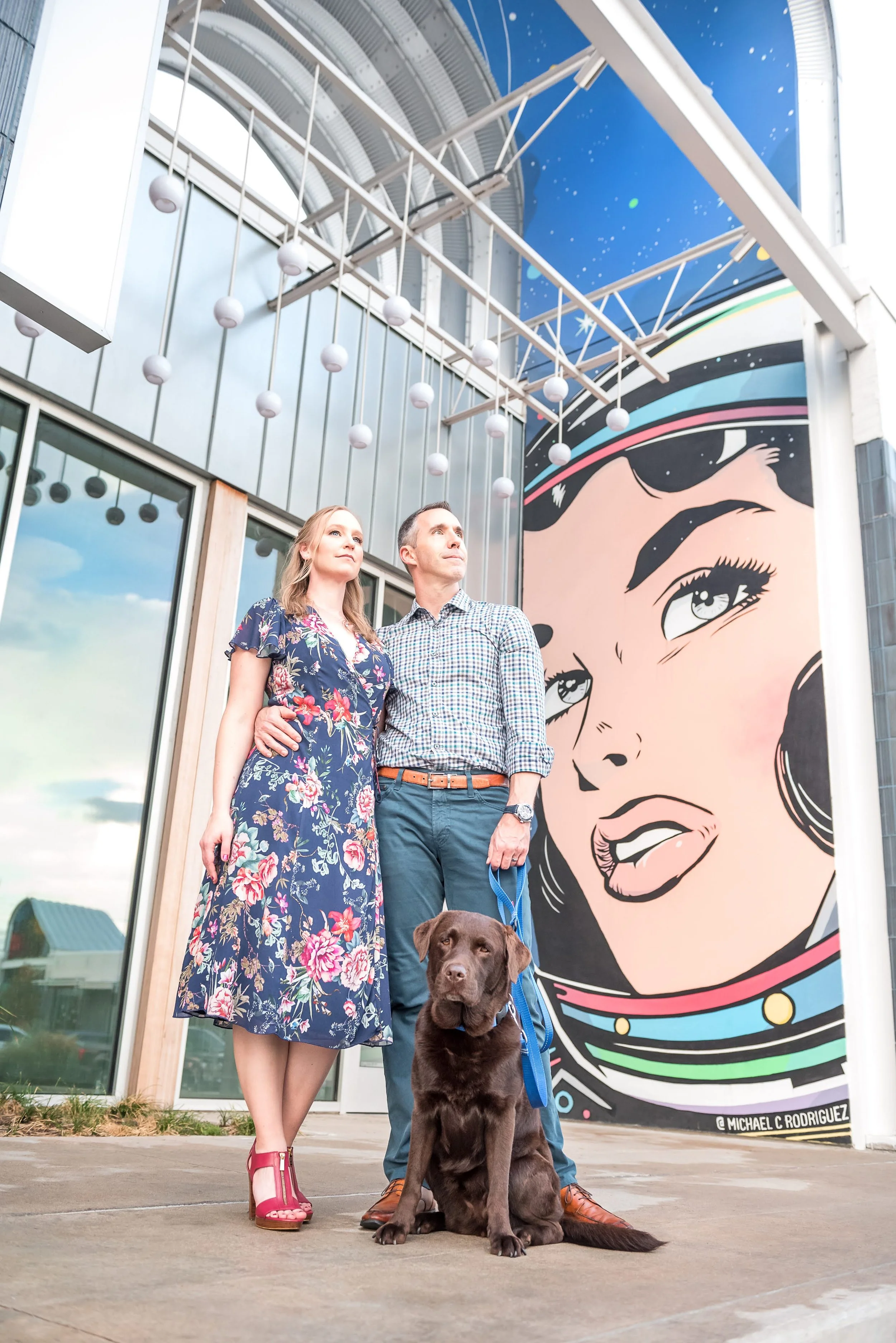A woman and man stand in front of a space-themed mural with a chocolate lab.
