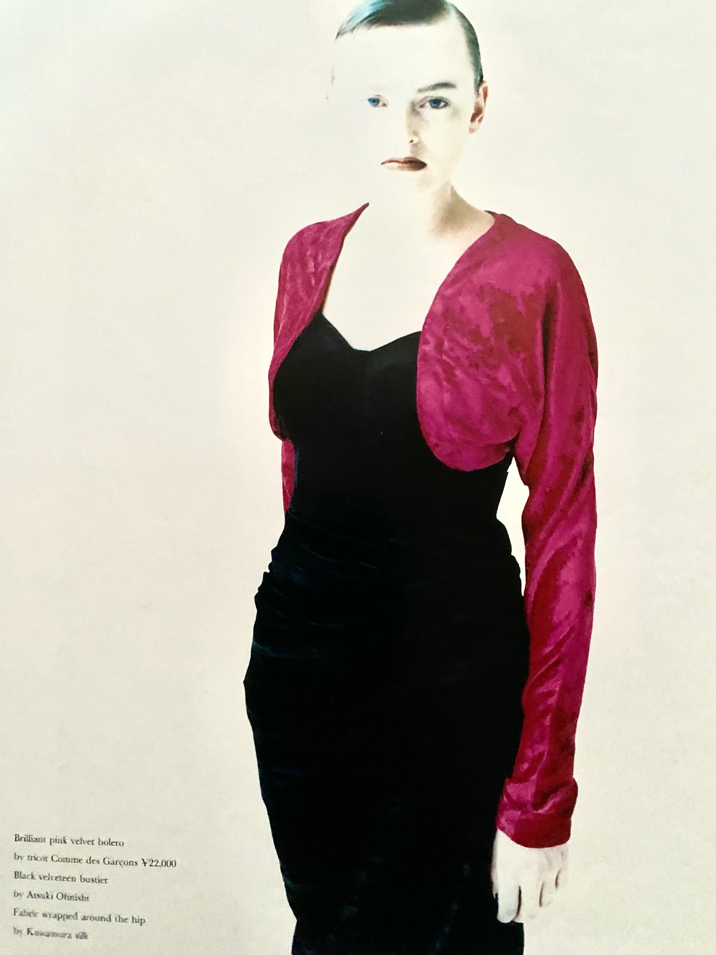 A woman with short hair wearing a black japanese vintage dress with a pink comme des Garcons vintage velvet bolero jacket.