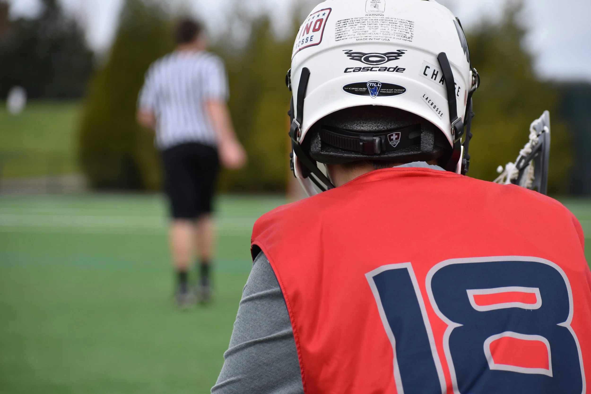 the back of a young lacrosse player with a referee in the background