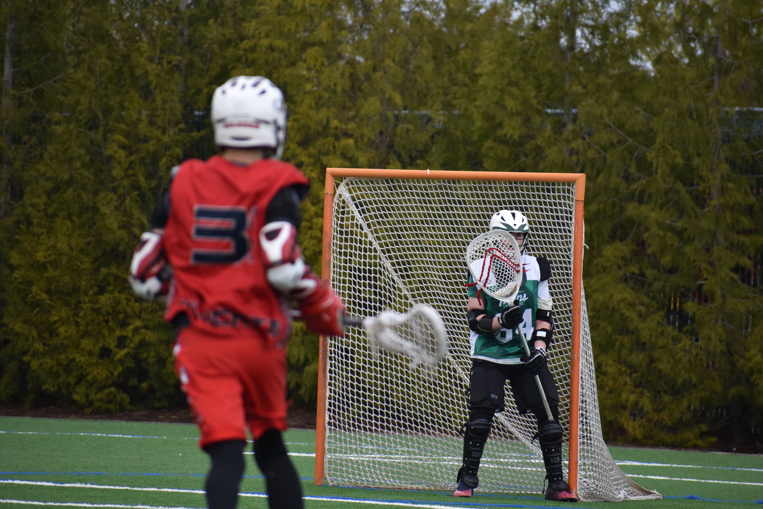 Young WYL player standing in front of a guarded lacrosse goal.