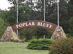 Sign reading 'Poplar Bluff,' with trees in the background and grass in the foreground.