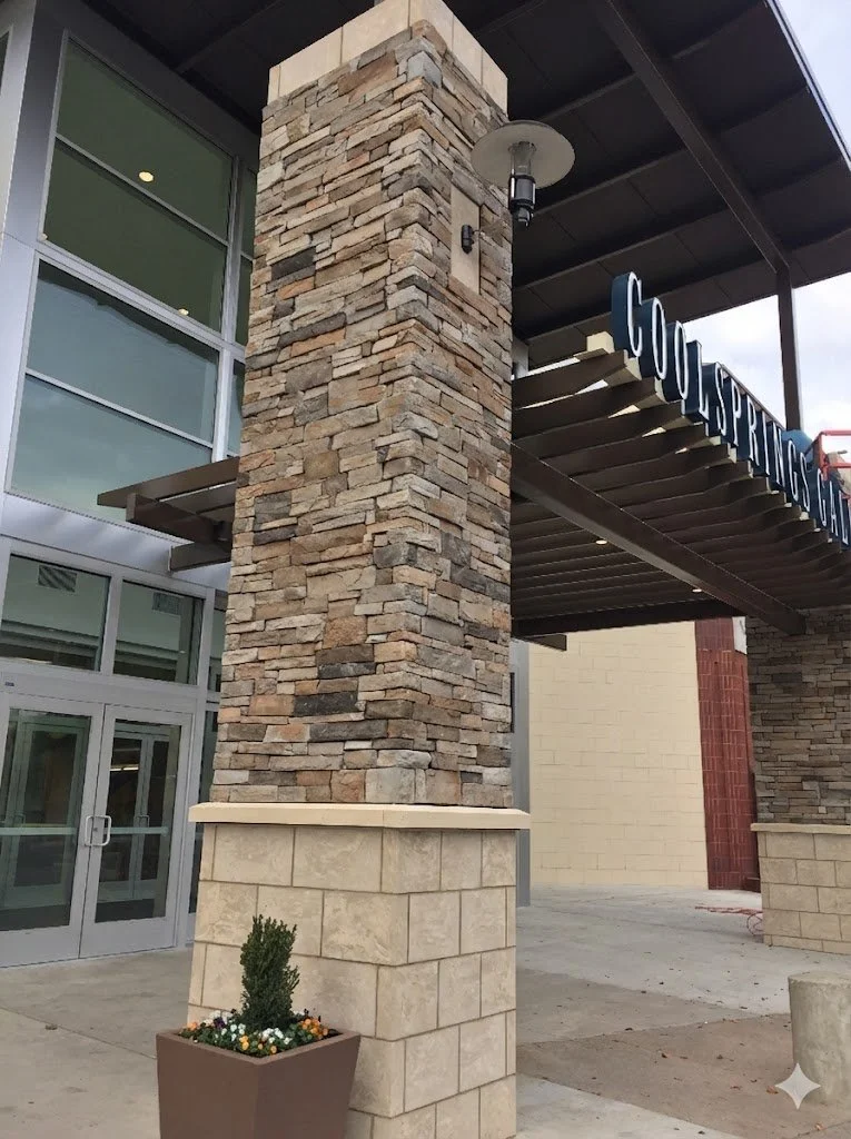 Exterior entrance of a building with large stone and brick column, glass doors, and a sign that says "GOURMET" partially visible.