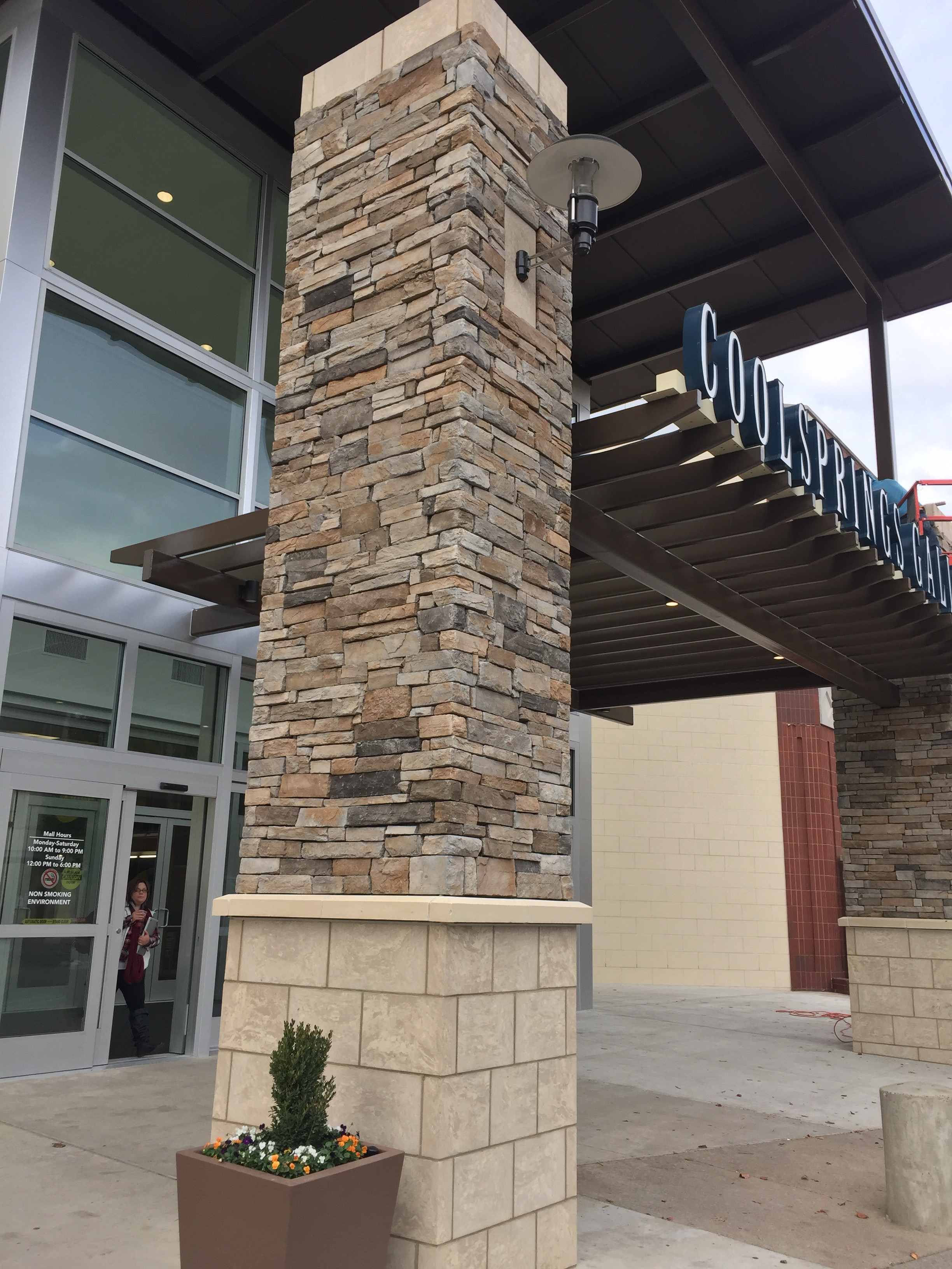 Exterior view of a shopping mall entrance with stone pillars, glass doors, and a sign that reads 'Goolspring'.