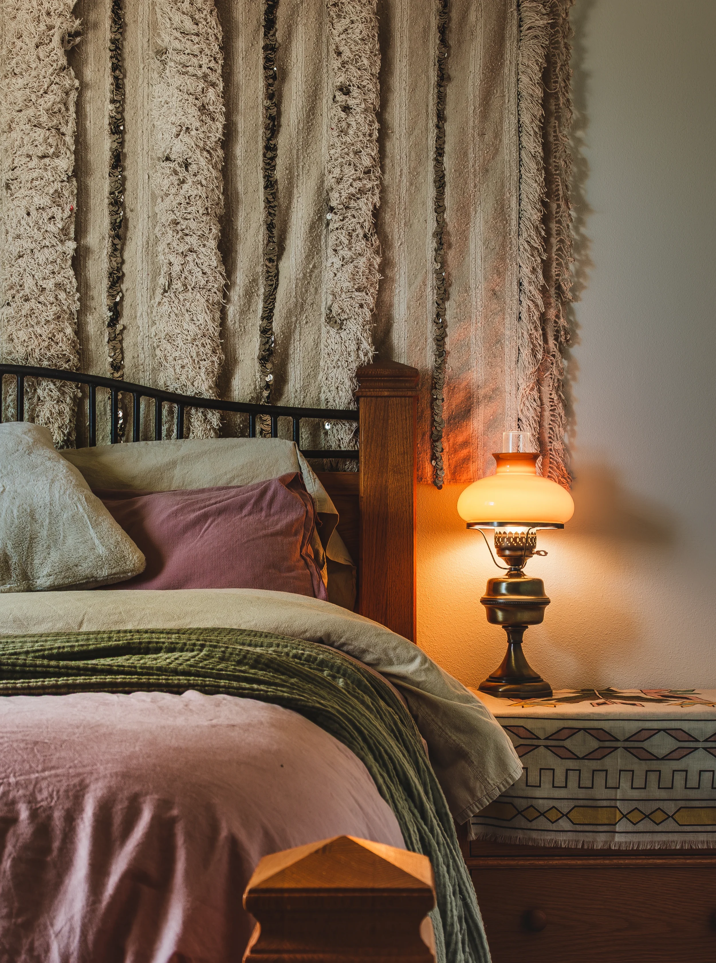 Cozy bedroom scene with a bed, decorative pillows, and a wooden nightstand with a vintage lamp, captured in Berthoud, Colorado.