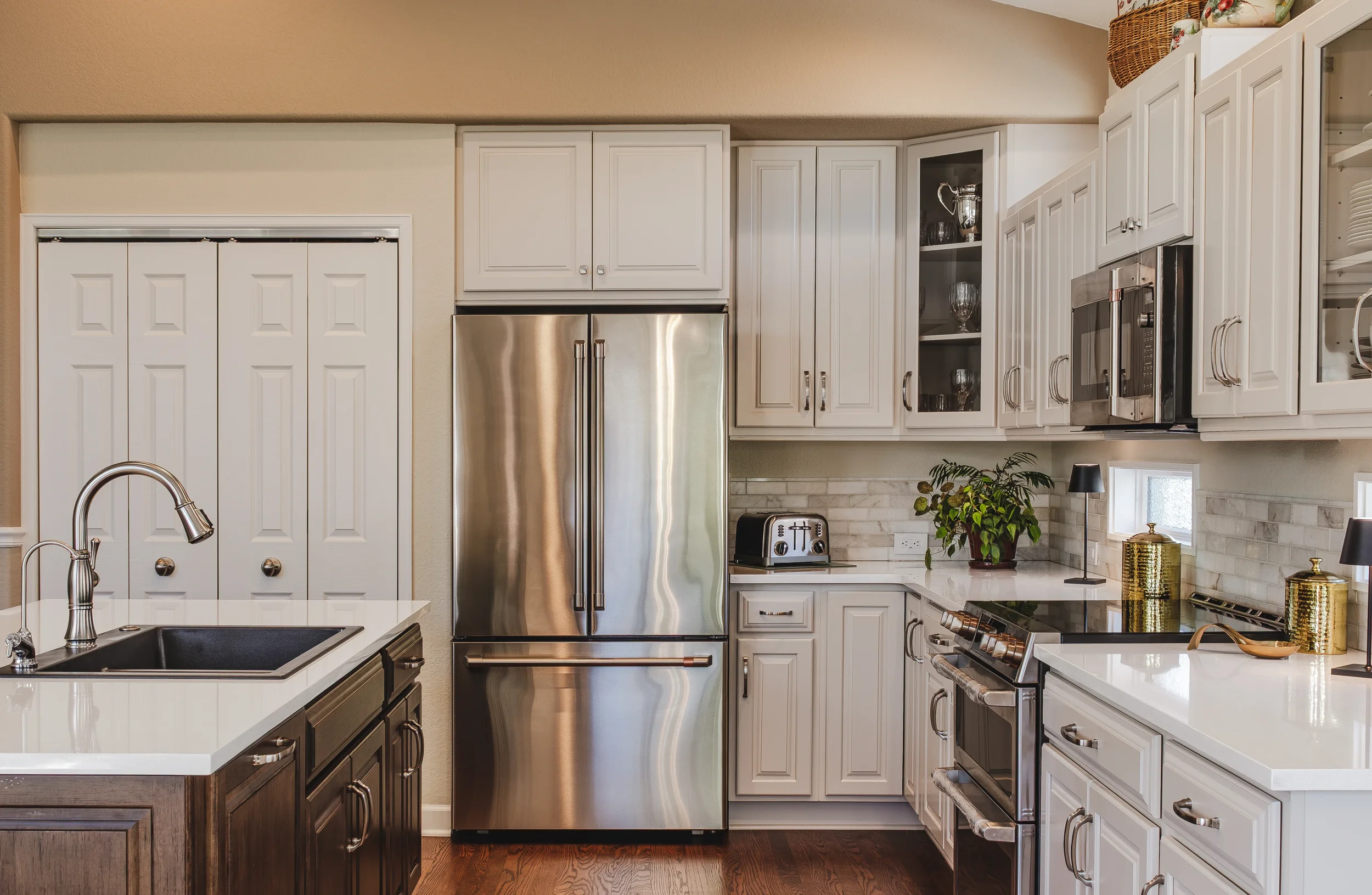 Architectural and Interior Design photo of a modern kitchen with white cabinets, stainless steel appliances, marble kitchen island, coffee maker, toaster, potted plant, and gold vases, taken in Longmont, Colorado by Context Images.