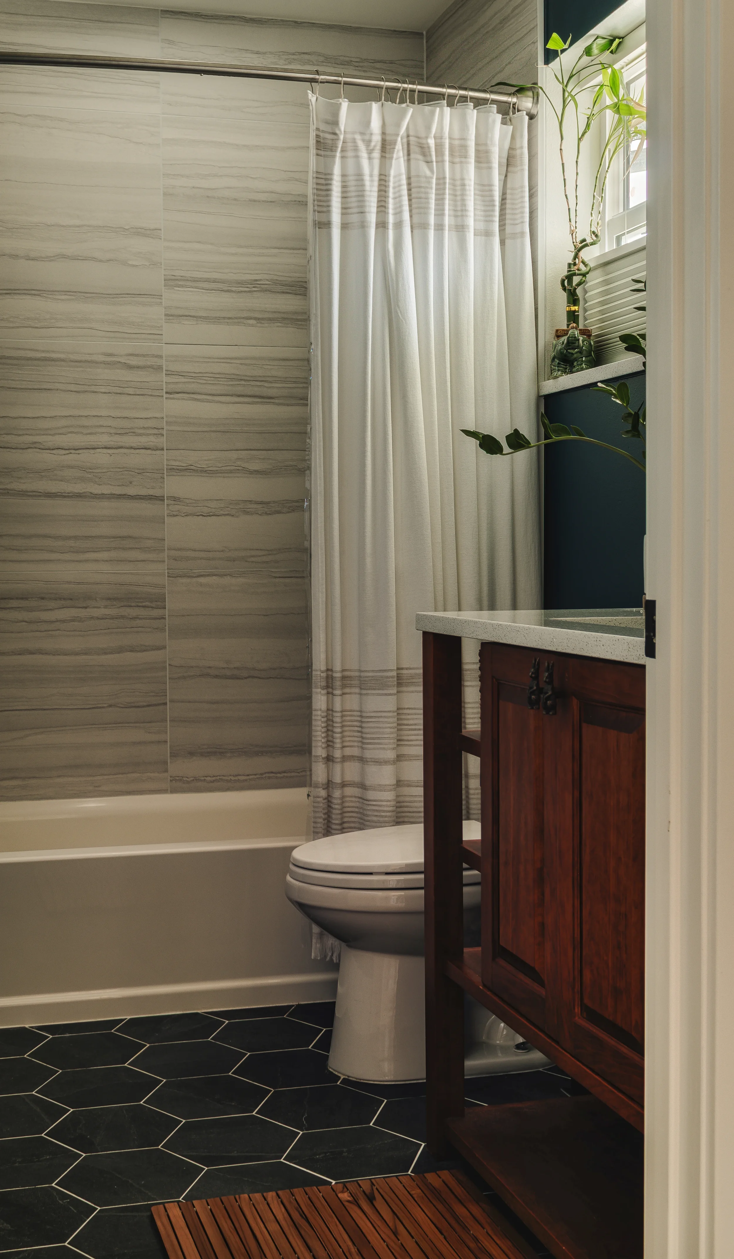 A small bathroom with a toilet, a wooden vanity, and a tiled wall in shades of gray, captured in Berthoud, Colorado by Context Images.