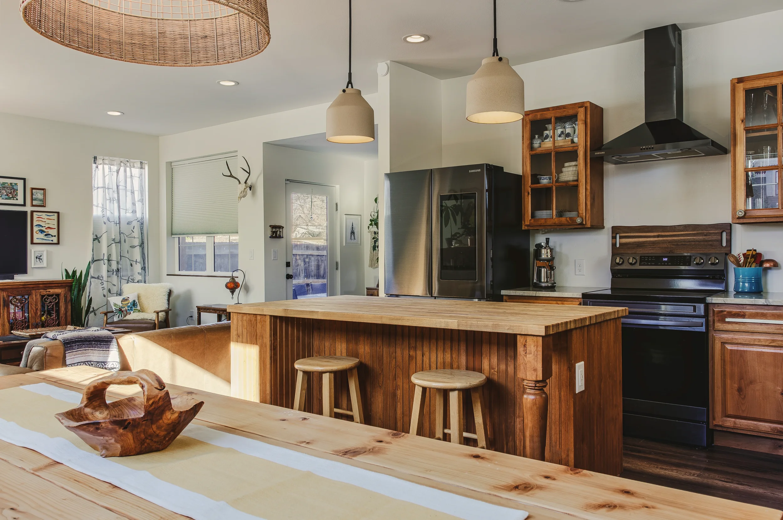 Warm open concept kitchen with wooden cabinets, black appliances, butcher block island, and a cozy sitting area in the living room shot by Context Images in Berthoud, Colorado.